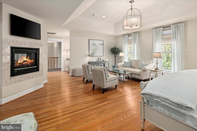 bedroom with light wood-style flooring, a tiled fireplace, baseboards, recessed lighting, and a raised ceiling