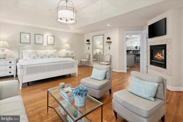bedroom featuring a raised ceiling, wood finished floors, a glass covered fireplace, and baseboards