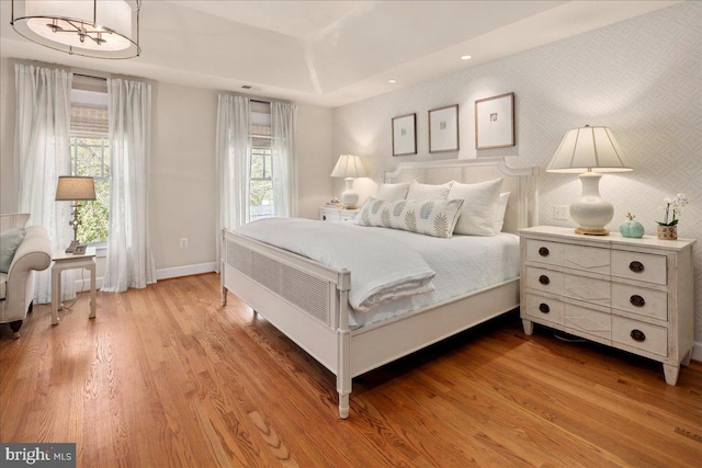 bedroom with baseboards, wood finished floors, wallpapered walls, and multiple windows