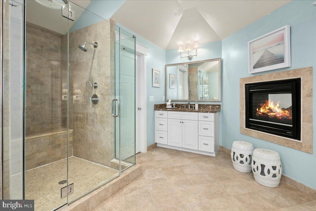 bathroom featuring a glass covered fireplace, vaulted ceiling, vanity, and a shower stall