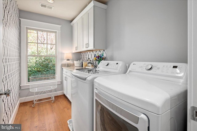 clothes washing area with light wood-style floors, cabinet space, washing machine and dryer, baseboards, and visible vents