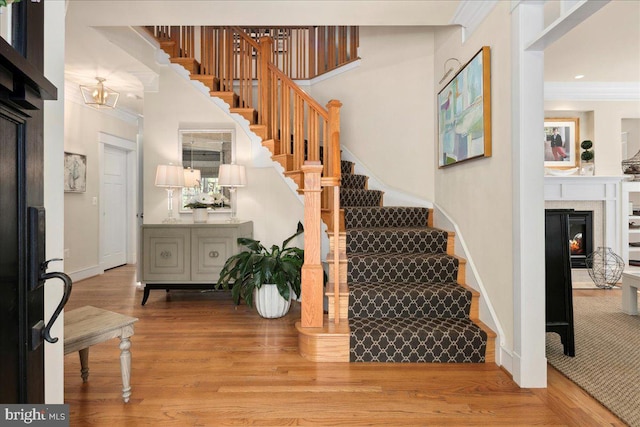 foyer entrance with stairway, wood finished floors, ornamental molding, baseboards, and a glass covered fireplace