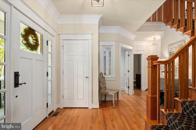 foyer entrance featuring stairway, visible vents, ornamental molding, light wood-type flooring, and a chandelier