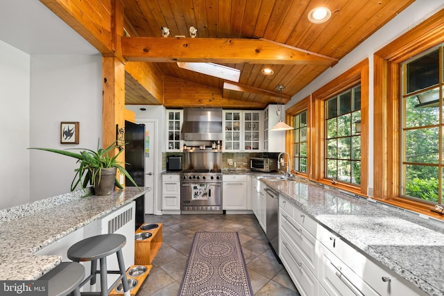 kitchen featuring wall chimney range hood, stainless steel appliances, glass insert cabinets, tasteful backsplash, and white cabinets