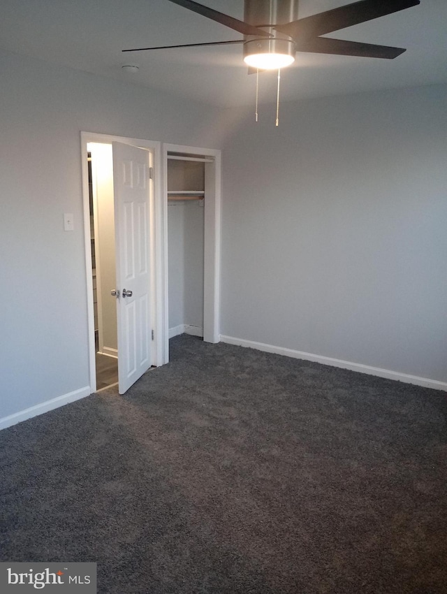 unfurnished bedroom with dark colored carpet, a closet, baseboards, and ceiling fan