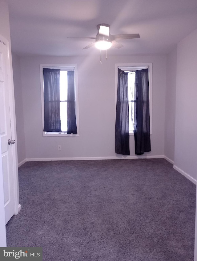 spare room with dark carpet, baseboards, and ceiling fan