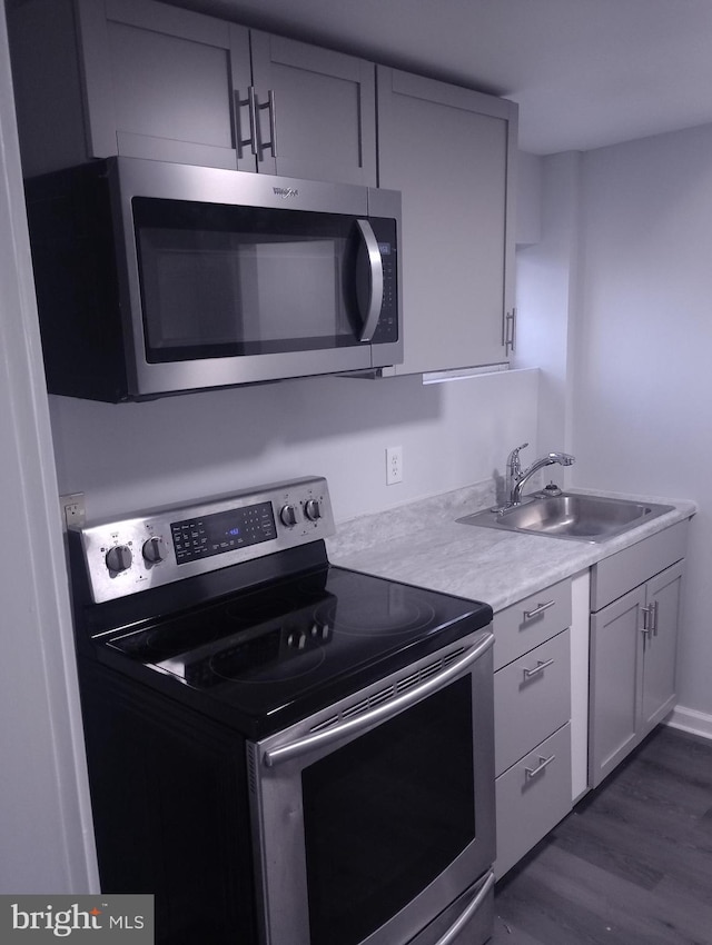 kitchen with light countertops, appliances with stainless steel finishes, dark wood-style floors, and a sink