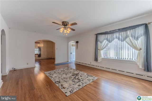 unfurnished living room with arched walkways, a ceiling fan, a baseboard heating unit, and a wealth of natural light