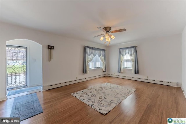spare room featuring baseboard heating, arched walkways, ceiling fan, and wood finished floors