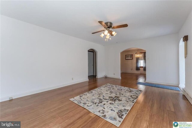 unfurnished living room featuring arched walkways, ceiling fan, baseboards, and wood finished floors