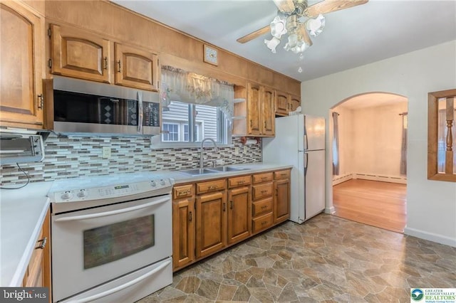 kitchen featuring a sink, white appliances, stone finish floor, arched walkways, and a ceiling fan
