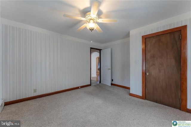 unfurnished bedroom featuring carpet floors, baseboards, a ceiling fan, and arched walkways