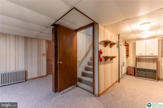 finished below grade area featuring a paneled ceiling, baseboards, radiator heating unit, carpet flooring, and stairs