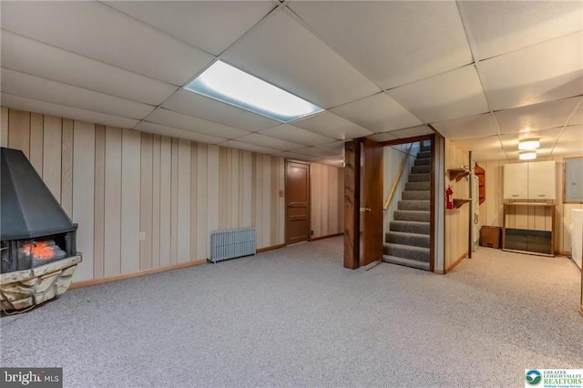 finished basement with a wood stove, carpet floors, radiator, stairs, and a drop ceiling