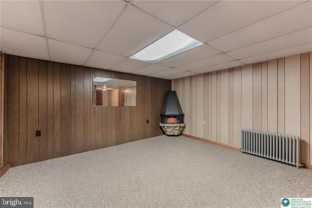finished below grade area featuring radiator heating unit, carpet floors, wood walls, and a paneled ceiling