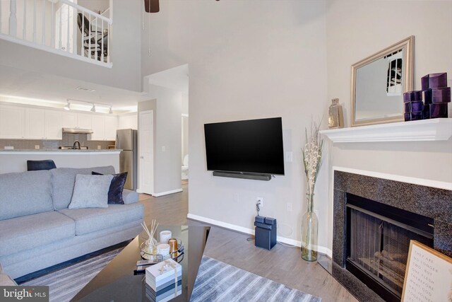 living room featuring a ceiling fan, a towering ceiling, a fireplace, wood finished floors, and baseboards