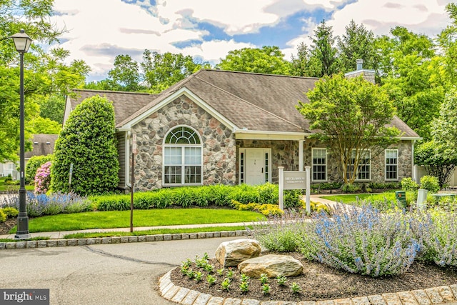single story home with a front lawn, roof with shingles, and stone siding