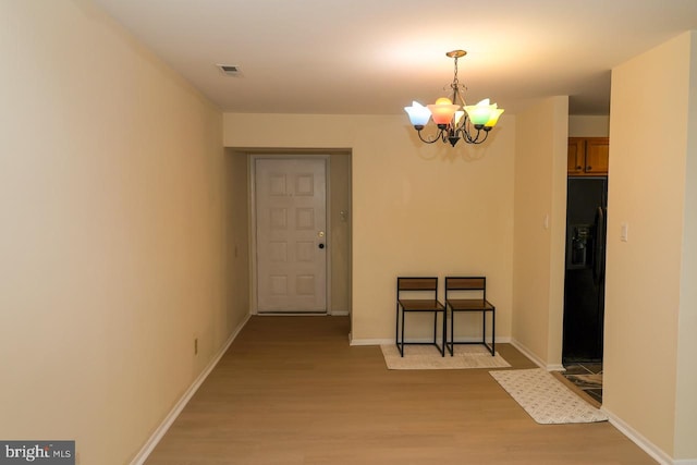 unfurnished dining area with a chandelier, light wood finished floors, and baseboards