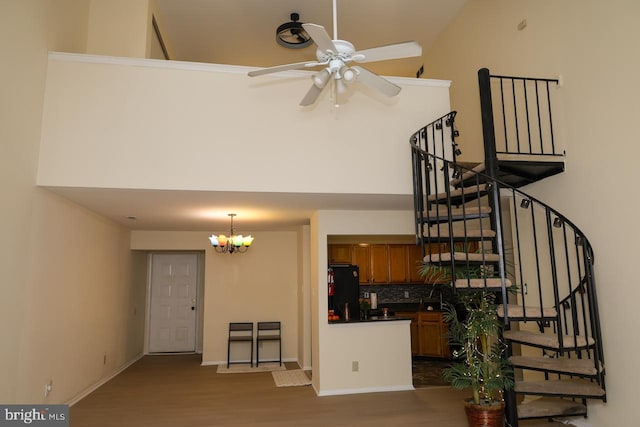 unfurnished living room with wood finished floors, ceiling fan, stairway, a chandelier, and baseboards