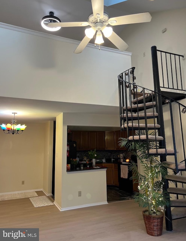 unfurnished living room featuring wood finished floors, stairway, a ceiling fan, baseboards, and ornamental molding