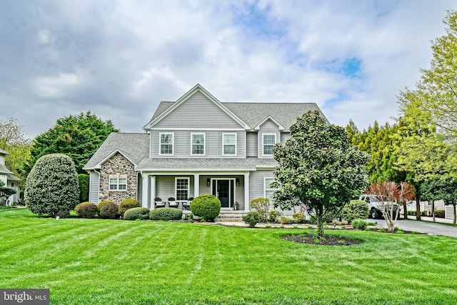 craftsman house with covered porch, a front yard, a shingled roof, and stone siding