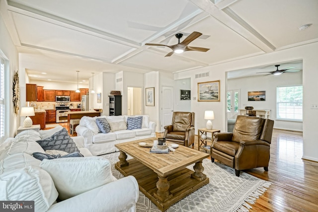 living area featuring light wood-style flooring, a ceiling fan, beamed ceiling, visible vents, and coffered ceiling