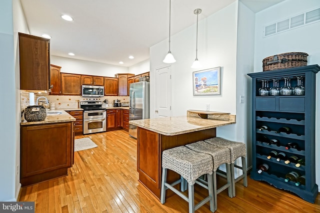 kitchen featuring appliances with stainless steel finishes, a sink, light wood-style floors, a peninsula, and visible vents