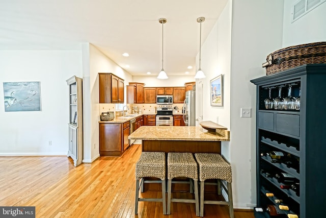 kitchen with brown cabinets, appliances with stainless steel finishes, a peninsula, light wood-type flooring, and visible vents
