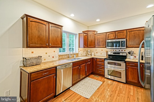 kitchen featuring backsplash, appliances with stainless steel finishes, light stone countertops, light wood-type flooring, and a sink