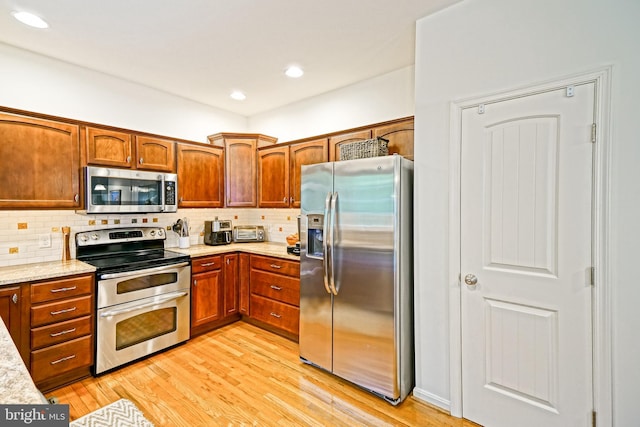 kitchen featuring brown cabinetry, backsplash, stainless steel appliances, and light wood-style flooring