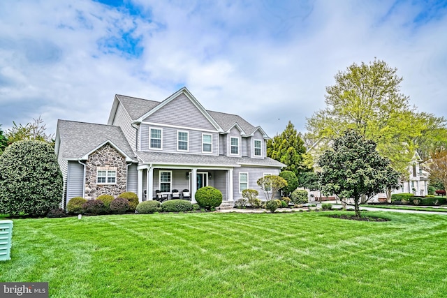view of front of home featuring a front yard, roof with shingles, covered porch, and stone siding