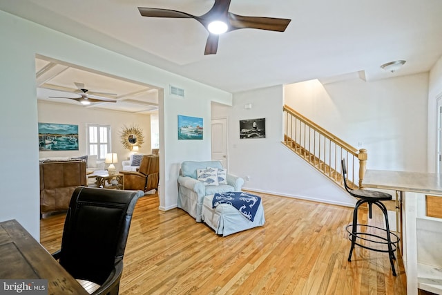 living room featuring visible vents, wood finished floors, baseboards, stairway, and a ceiling fan