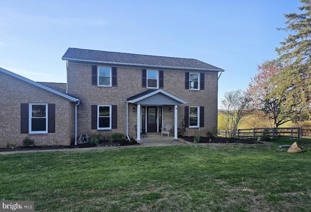 colonial home with fence, a front lawn, and brick siding