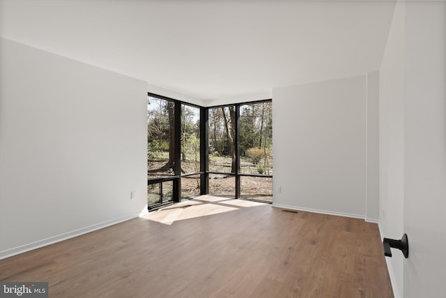 spare room featuring a wall of windows, wood finished floors, visible vents, and baseboards