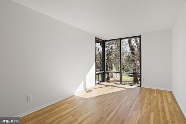 spare room featuring visible vents, baseboards, a wall of windows, and wood finished floors