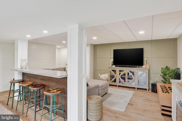 living room with recessed lighting, wood finished floors, a decorative wall, and a dry bar