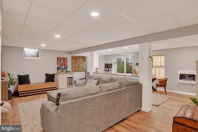 living room with heating unit, light wood-type flooring, a drop ceiling, and baseboards