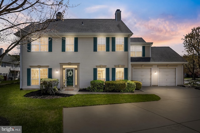 colonial inspired home featuring a chimney, a front lawn, driveway, and an attached garage