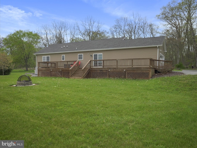 rear view of property featuring a shingled roof, an outdoor fire pit, a yard, and a deck