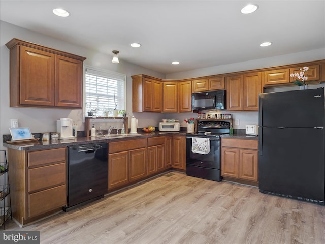 kitchen featuring light wood-style flooring, brown cabinetry, black appliances, dark countertops, and a sink