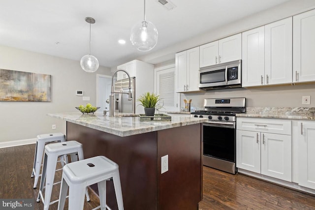 kitchen featuring dark wood-style flooring, stainless steel appliances, white cabinets, and light stone counters