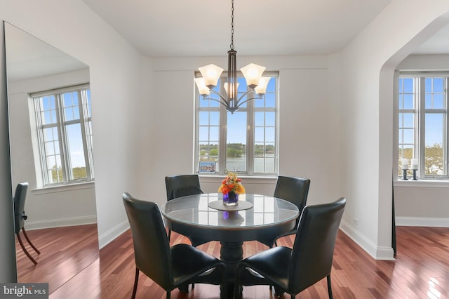 dining space featuring a chandelier, wood finished floors, arched walkways, and baseboards