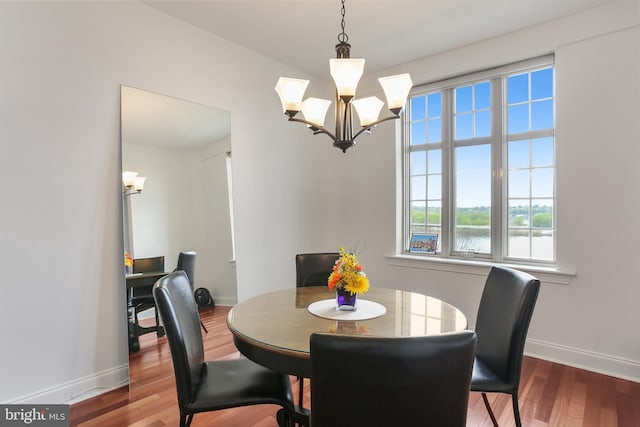 dining space featuring an inviting chandelier, wood finished floors, a water view, and baseboards