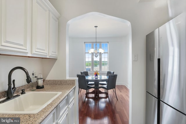 kitchen featuring dark wood-style floors, a sink, freestanding refrigerator, a notable chandelier, and white cabinetry