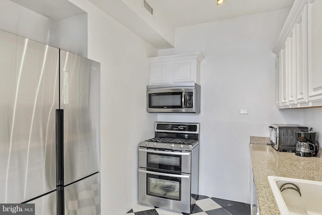 kitchen featuring tile patterned floors, a sink, visible vents, white cabinetry, and appliances with stainless steel finishes