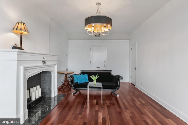 sitting room featuring baseboards, wood finished floors, a chandelier, and a fireplace with raised hearth