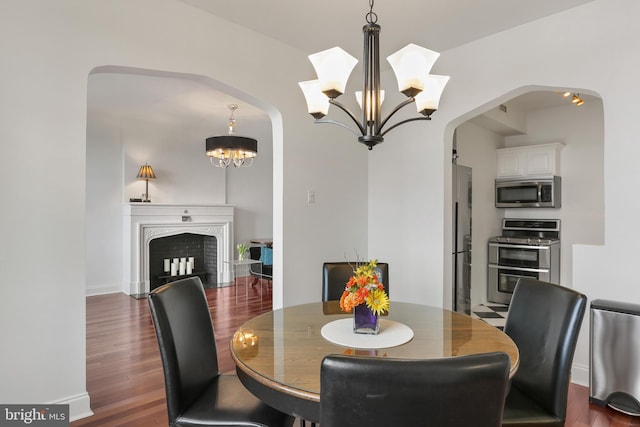 dining room featuring arched walkways, baseboards, dark wood-style flooring, and an inviting chandelier