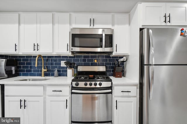 kitchen with white cabinets, stainless steel appliances, a sink, decorative backsplash, and light stone countertops
