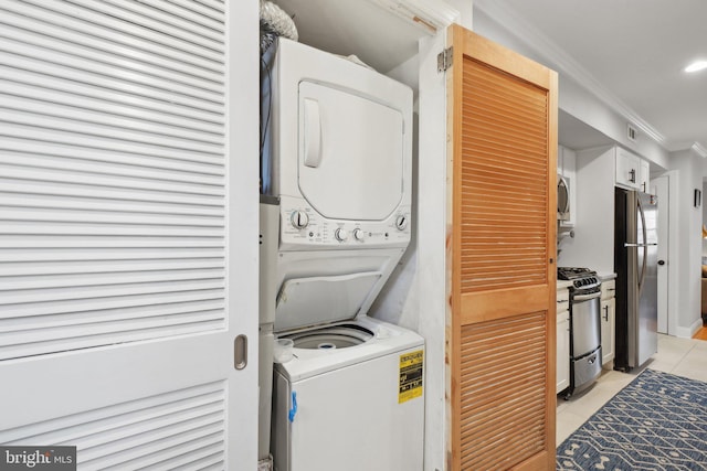 clothes washing area featuring light tile patterned floors, stacked washer and dryer, laundry area, and ornamental molding