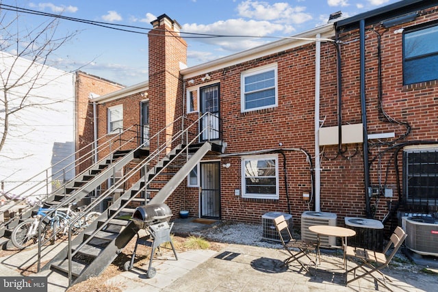 rear view of property with brick siding, cooling unit, and a patio